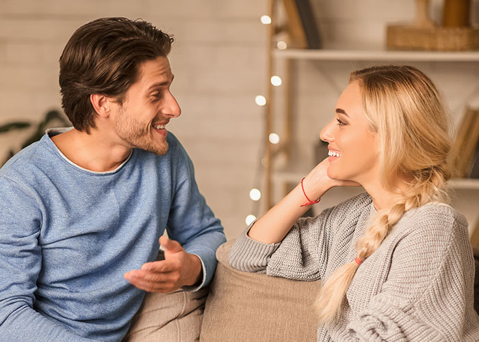 Couple smiling and chatting on a cozy sofa, discussing a public proposal turned private conversation.