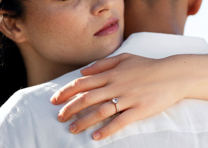 Woman with engagement ring embracing a partner, contemplating acceptance of a public proposal.