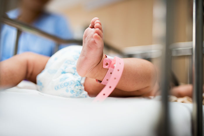 Baby lying in hospital crib with a pink ID band around its ankle.