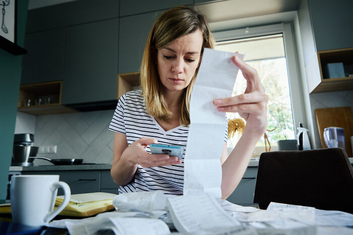 Woman reviewing receipts in kitchen, scrutinizing expenses as middle class costs rise.