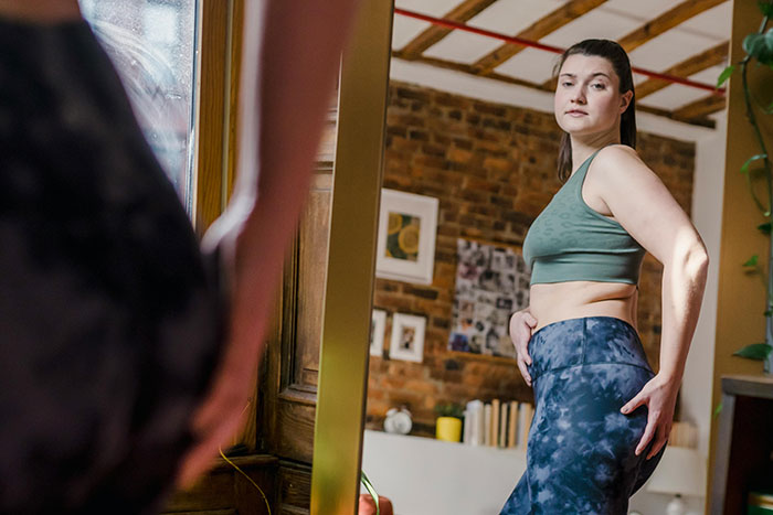 Woman in workout clothes looking at herself in the mirror, reflecting on Ozempic butt side effect.