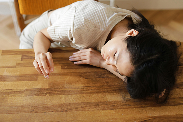 Pregnant woman in a beige dress lying on a wooden table, resting peacefully.