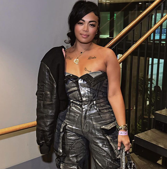 Woman in a metallic jumpsuit and jacket on stairs, related to flight attendant's lingerie business and GoFundMe support.