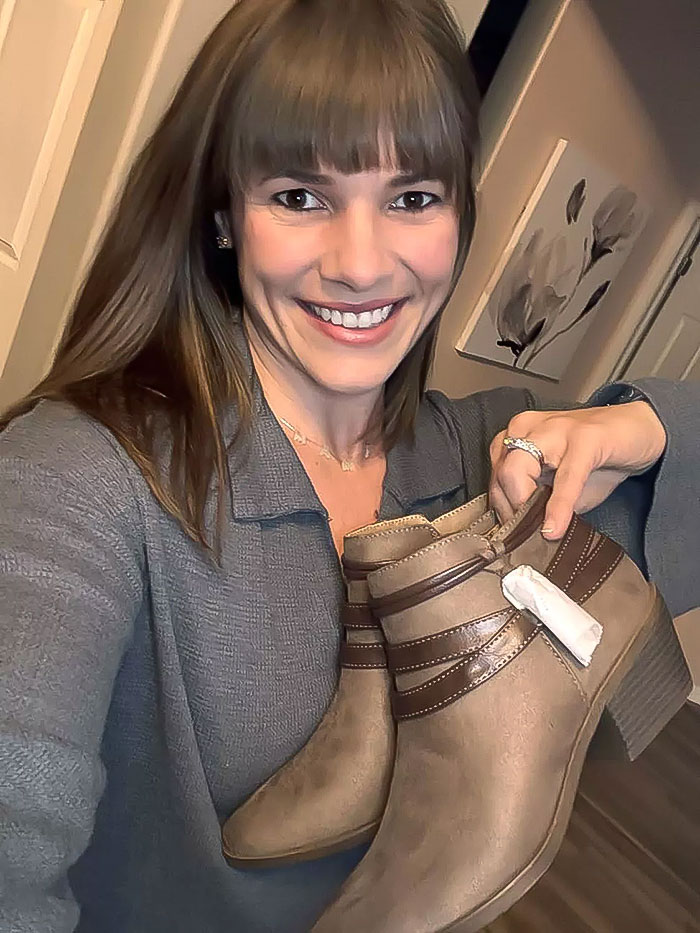 Woman smiling and holding thrifted boots with tags, representing a gift for her MIL.