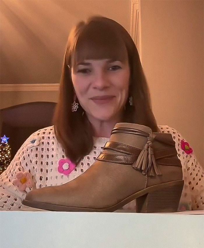 Woman holding thrifted boots as a gift, smiling in a cozy setting with holiday decor.