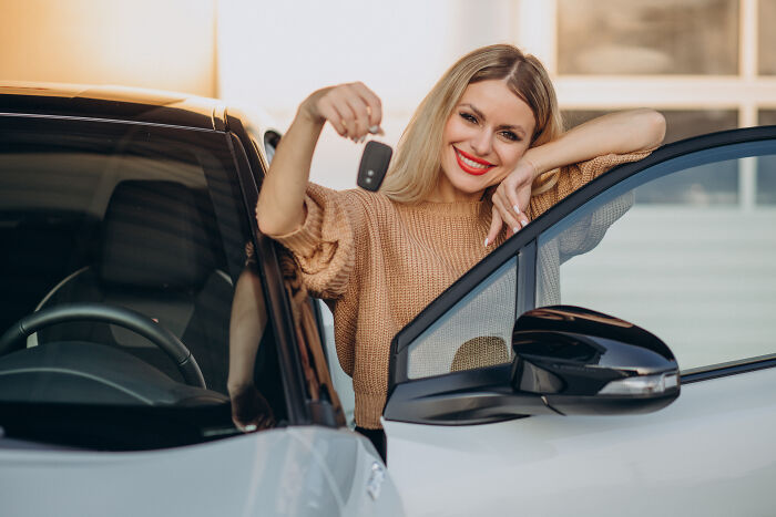 Woman smiling while holding car keys in front of vehicle, symbolizing unaffordable costs for the middle class.