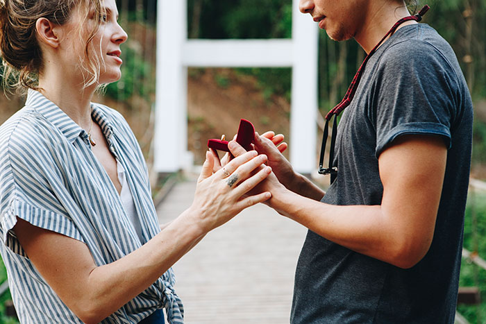 A man proposing to his best friend with a ring in a park setting.