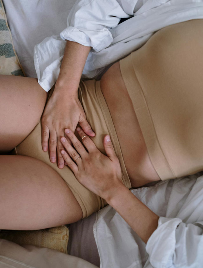 Woman lying on a bed with hands on her abdomen, expressing contemplation over future <a target=