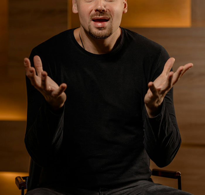 Man in a black shirt gesturing with open hands, discussing hysterectomy and surrogacy pressures.