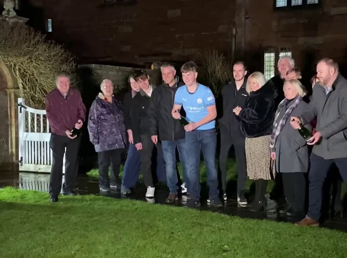 Group celebrating lottery win with champagne bottles, standing in a garden at night.