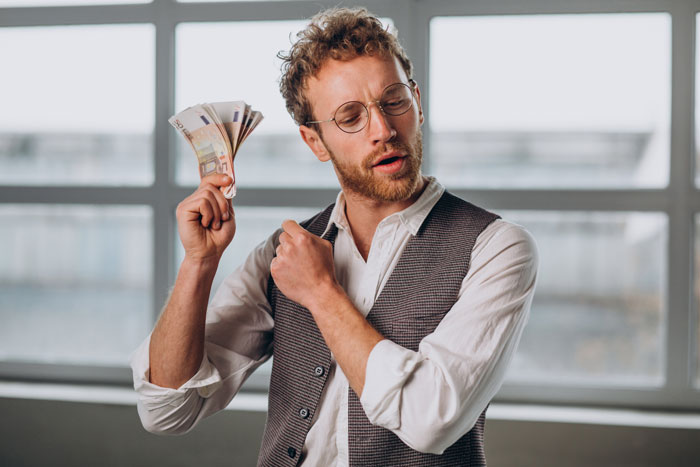 Man holding euros confidently in an office, symbolizing lottery win, reflecting on his engineer work commitment.