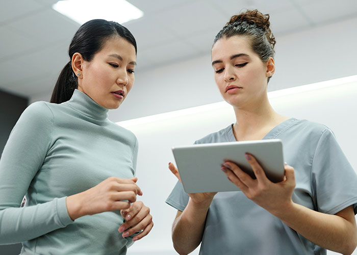 Two healthcare professionals discussing patient information on a tablet in a clinical setting.