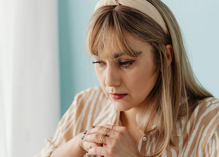 A worried woman with blonde hair and striped shirt contemplates American healthcare challenges.