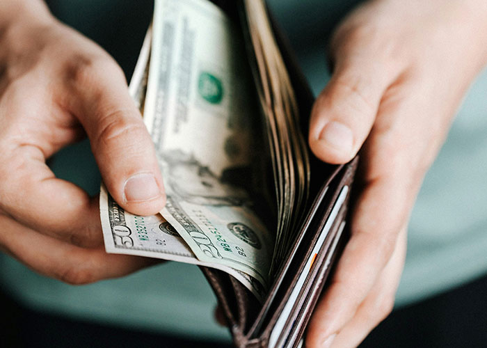 Hands holding a wallet with dollar bills, illustrating American healthcare costs.