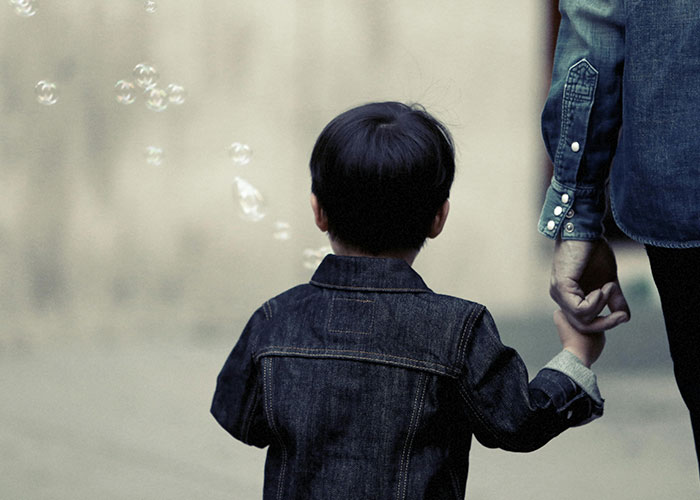 Child holding hand, bubbles in background, evokes stories about American healthcare's challenges.