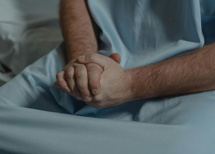 Person in a hospital bed with hands clasped, representing American healthcare challenges.