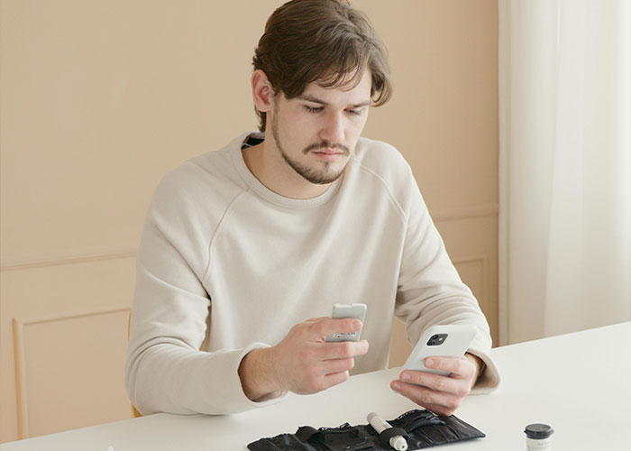 Man in a beige sweater checks phone, illustrating American healthcare experiences.