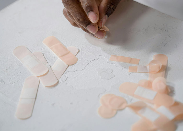 Person applying bandages, highlighting American healthcare challenges, with several adhesive strips on a white surface.