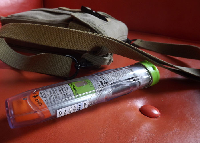 EpiPen on a red surface next to a brown bag, highlighting American healthcare issues.