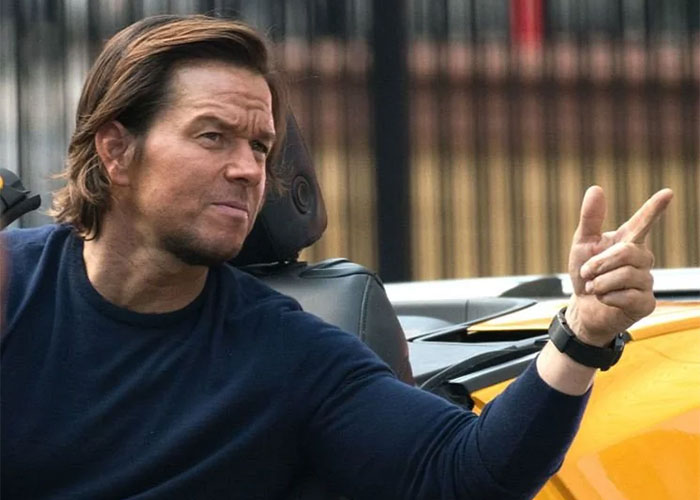 A man in a car gestures with his hand, wearing a navy blue shirt, relating to film snobs and casting in Hollywood.