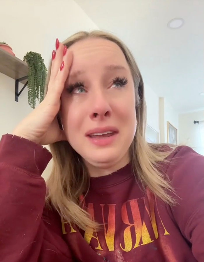 Person reacting emotionally to US TikTok ban news, wearing a red sweater indoors.