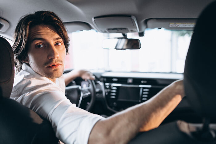 Man in white shirt, driving, looking back. Engaging non-sexual action.