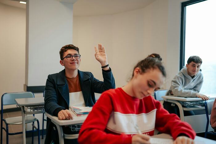 A millennial in a classroom raising his hand, symbolizing modern adulthood challenges and learning.