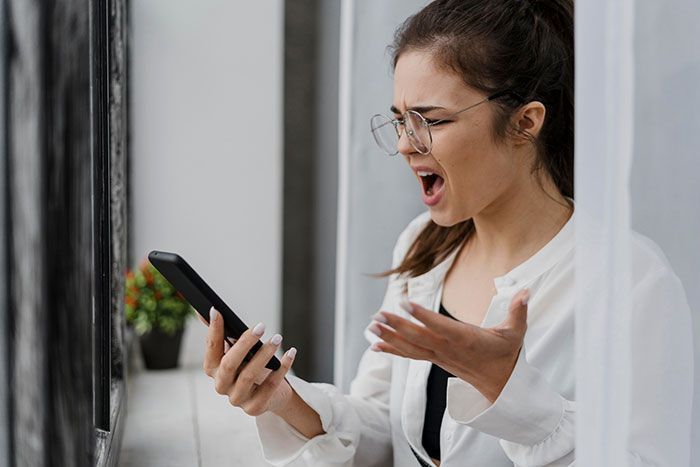 A woman in glasses looks frustrated while holding a phone, connected to an influencer controversy over free painting demands.