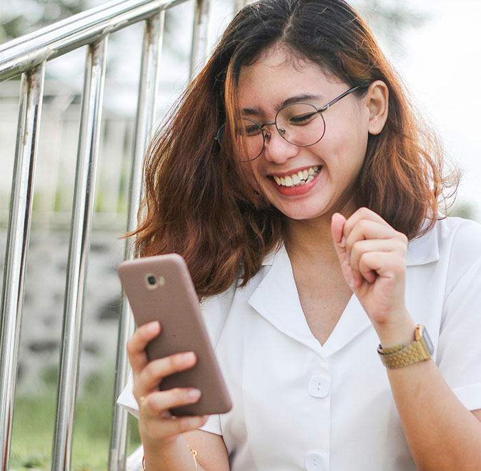 Woman smiling at her phone, representing "brain rot speak" concept.