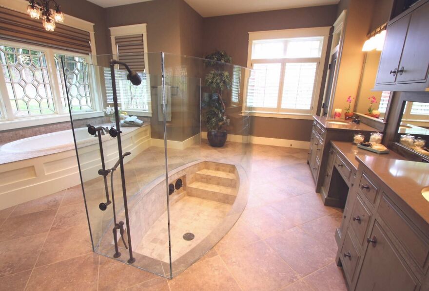 Unusual bathroom design with a sunken shower enclosed by glass, featuring contrasting tile and brown cabinets. Architecture shaming.