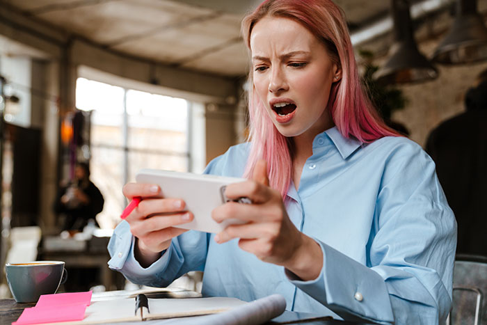 Woman surprised while checking her phone, reacting to last-minute vacation expense issues.