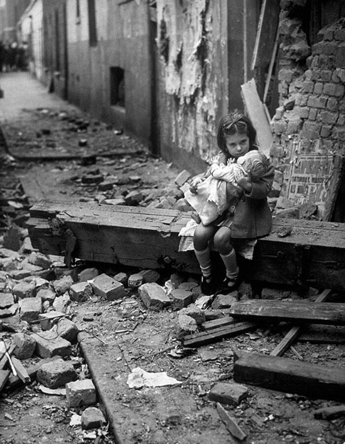 Young girl holding a doll, sitting amid war-torn rubble, symbolizing rare historical moments of resilience and hope.