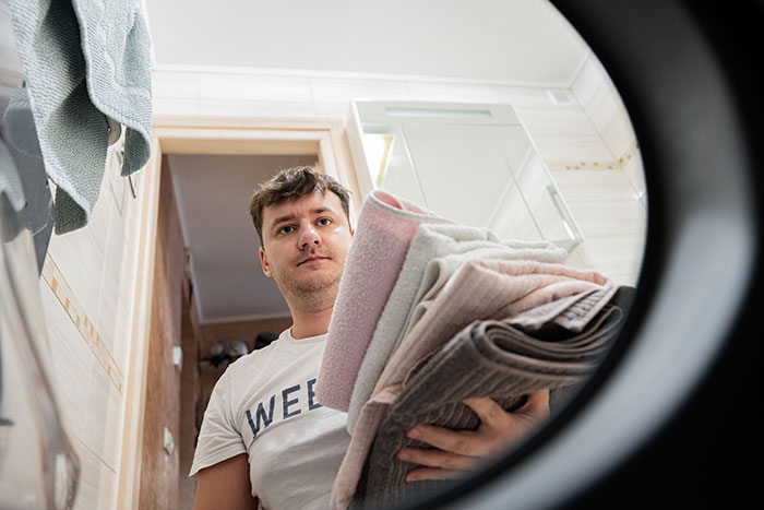 Man doing laundry at home, viewed from inside a washing machine.