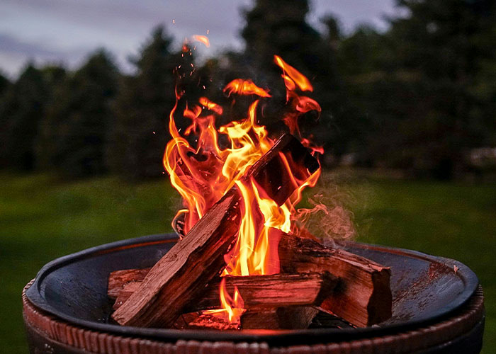 Fire pit burning in a yard with trees in the background, illustrating neighbor's logic in personal outdoor space use.