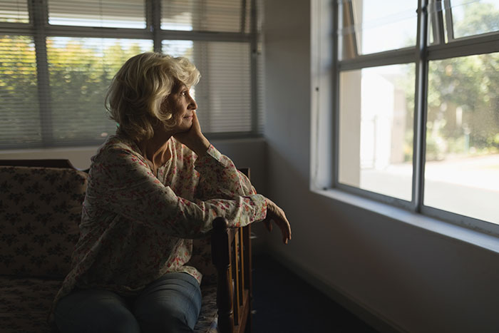 Woman contemplating by a window, concerned about inheritance decision favoring brother.