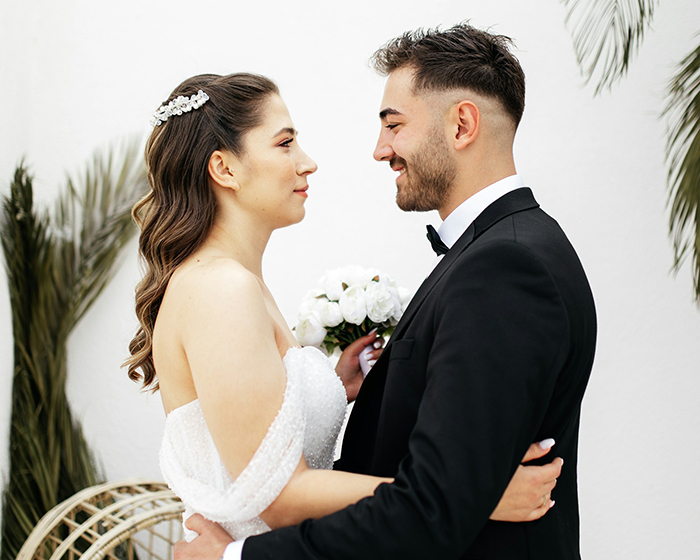 A bride and groom stand close, gazing at each other, surrounded by lush greenery, in a moment of joy and connection.