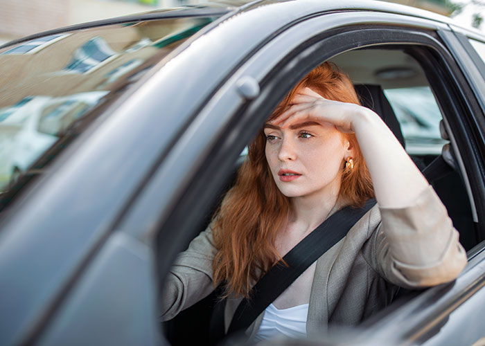 Person sitting in a car looking frustrated, possibly dealing with an entitled neighbor issue over parking.