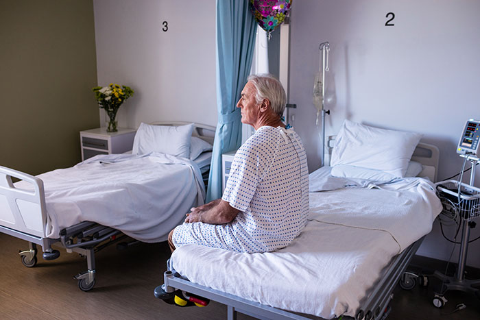 Elderly man in hospital gown sitting on bed in a hospital room.