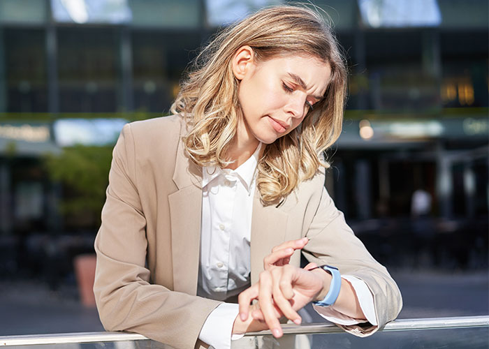 Woman looking at her watch, appearing stressed about time, outdoors in business attire.