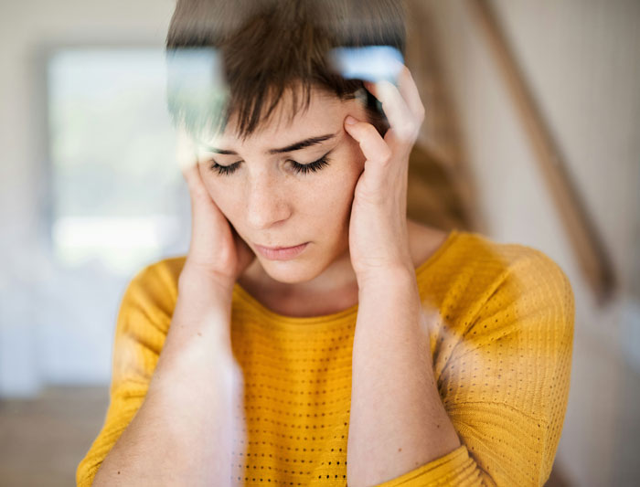 Woman in yellow sweater looking stressed, reflecting on children's well-being.