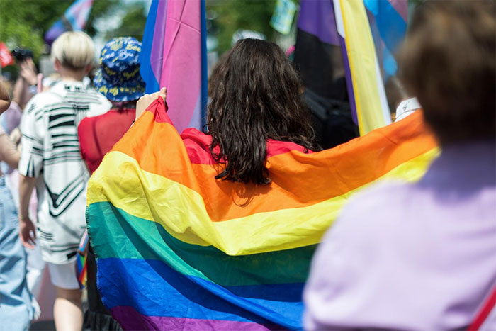 Person holding a rainbow flag at a pride event, surrounded by others celebrating LGBTQ+ rights.