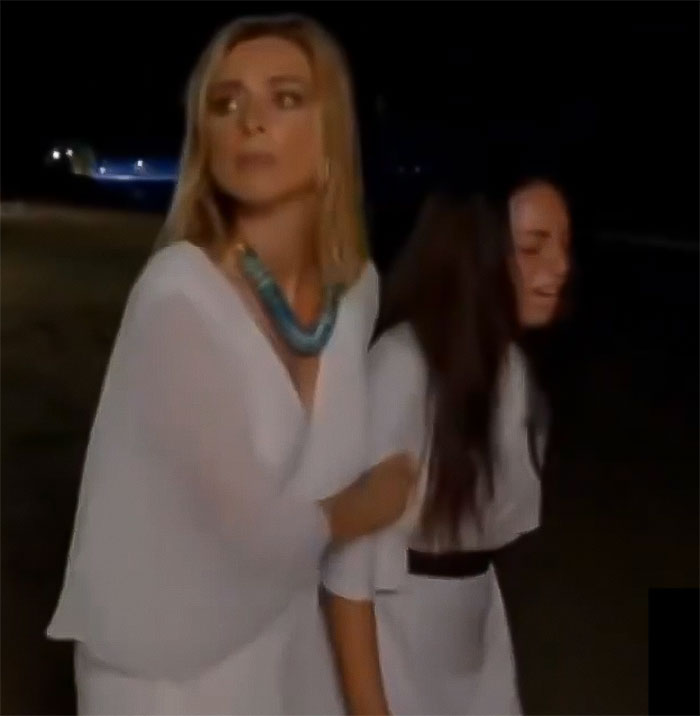 Women in white dresses during a reality show scene, appearing tense.