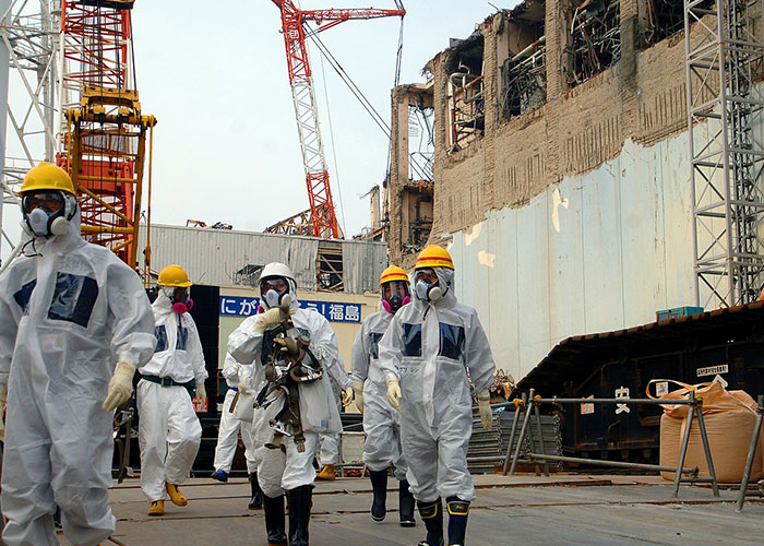 Workers in protective gear near a damaged building site with cranes in the background.