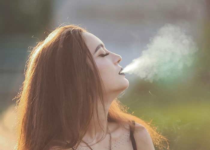 Woman outdoors exhaling smoke, highlighting Europe culture shocks experienced by Americans.