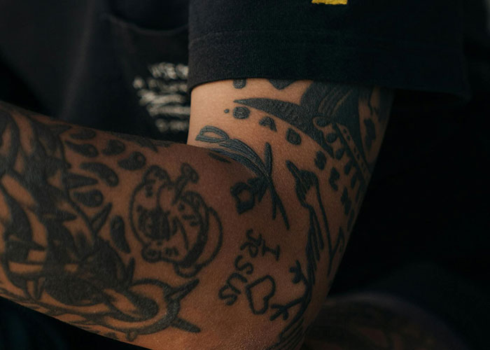 Close-up of an arm with various black tattoos, showcasing detailed ink art and designs.