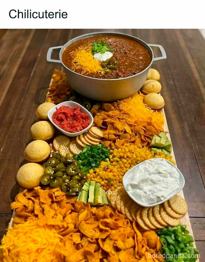 Cooking enthusiasts will enjoy this chili spread with various toppings and sides artfully arranged on a wooden board.