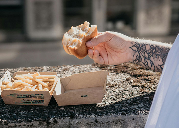 Tattooed arm holding a burger with fries, emphasizing considerations before getting inked.