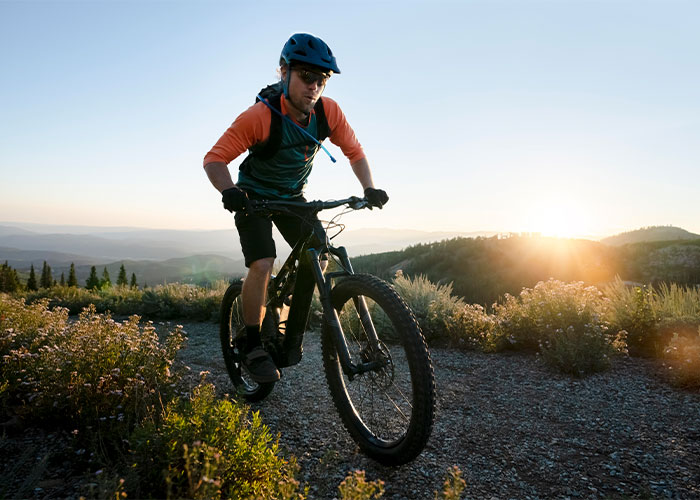 Cyclist riding on a trail during sunset, surrounded by mountains and greenery, symbolizing a scary hiking adventure.