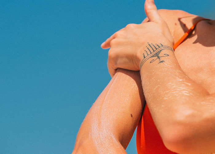 Person applying sunscreen, showing a wrist tattoo, a reminder to consider before getting inked.