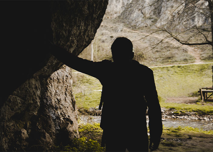 Silhouette of a person hiking near a rocky cave entrance, depicting one of the scariest hikes.